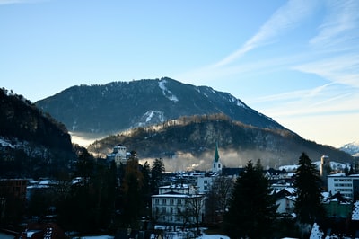 白色和黑色绿色树木和山附近的混凝土建筑在蓝天白天
